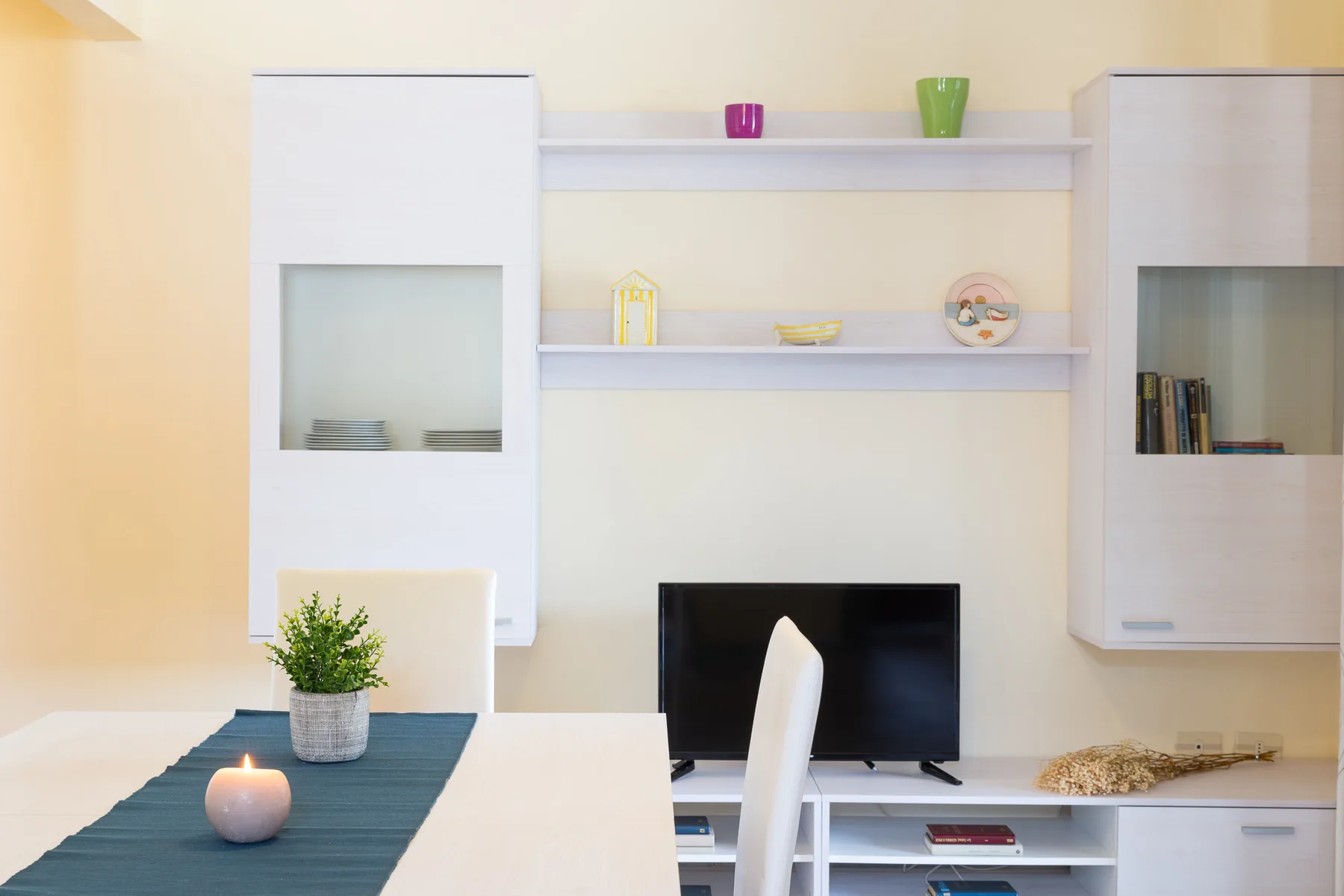 A bright living area with a television, built-in shelves, and a dining table.