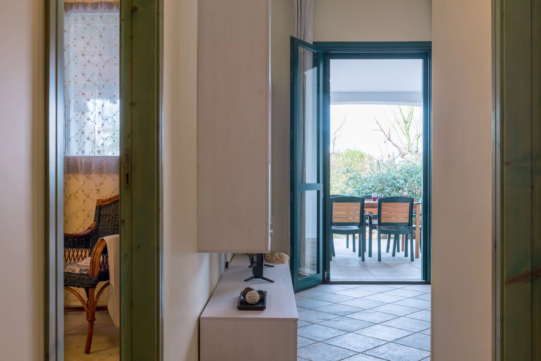 A tiled hallway opens onto a patio with a table and seating.