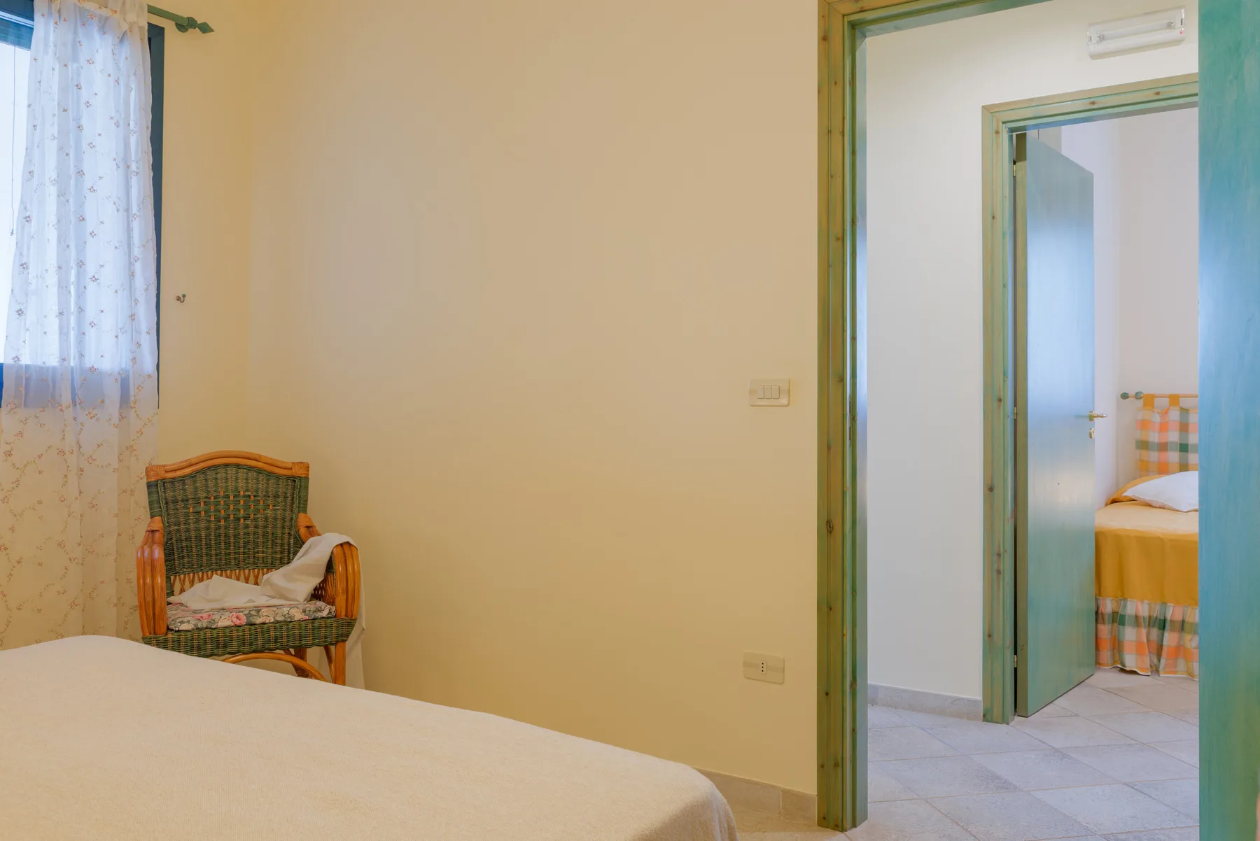 A bedroom with a bed, a wicker chair, and a doorway to another room.