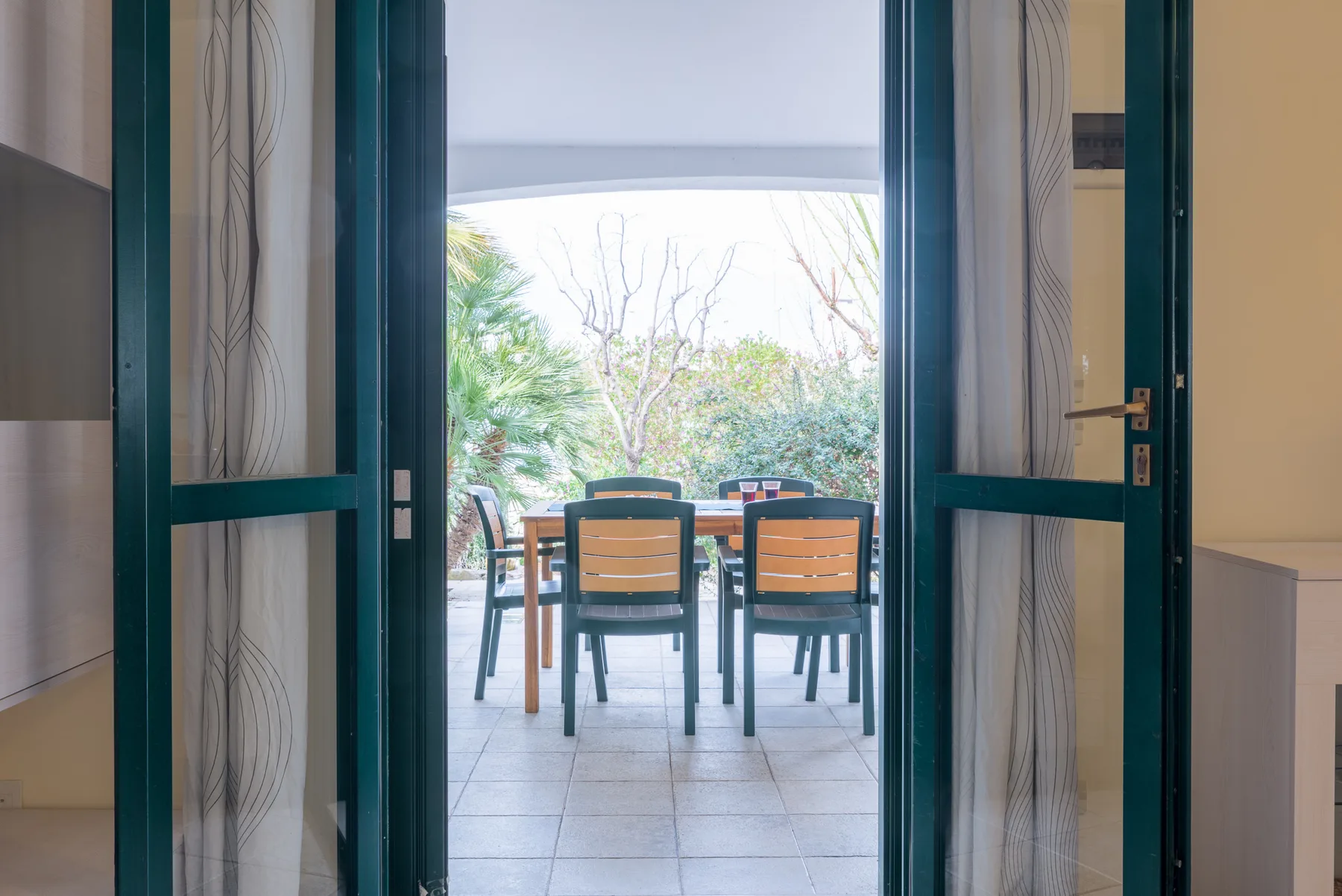 An open doorway looks onto an outdoor dining area with chairs and greenery.