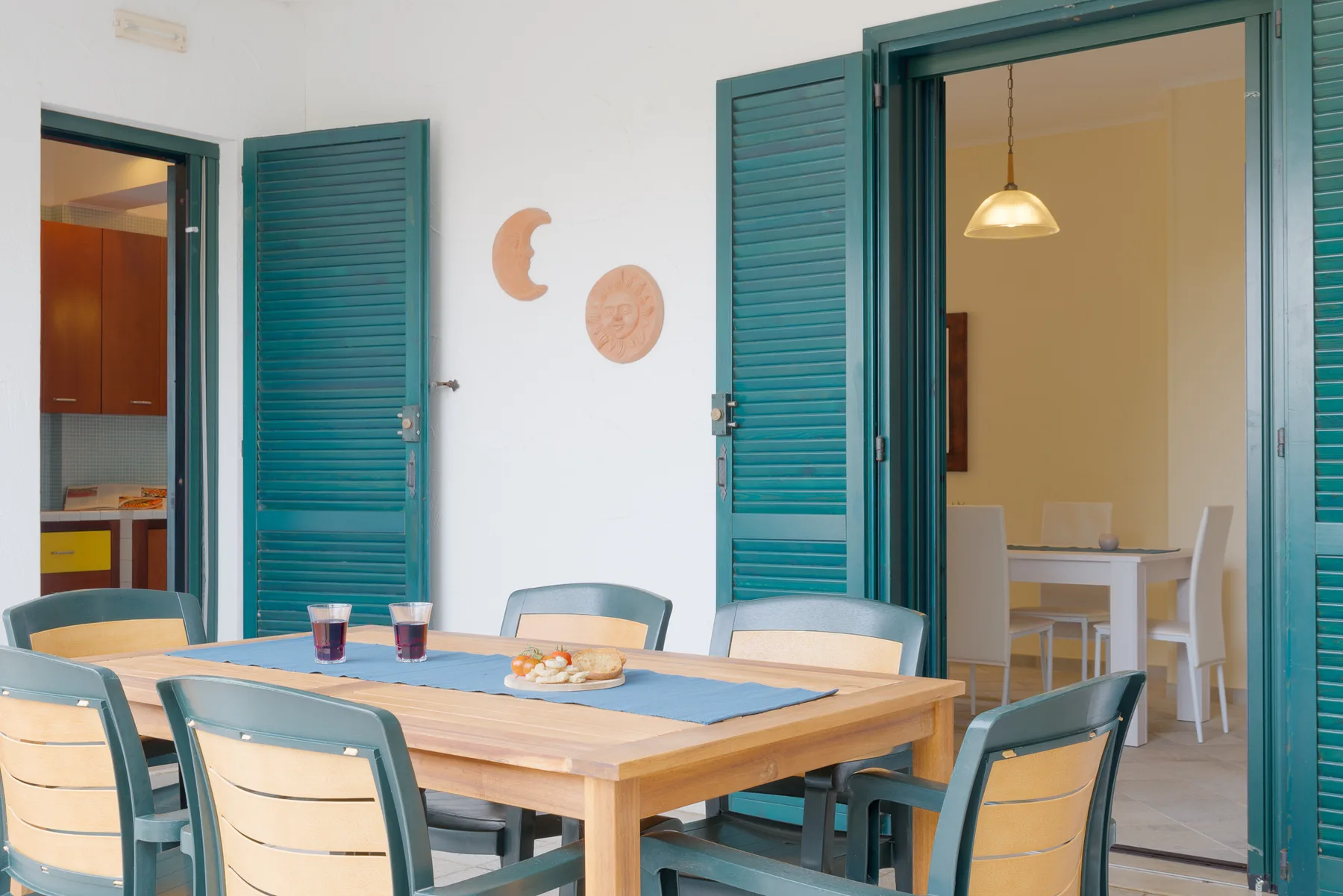 A dining area with a wooden table set beside open teal shutters.