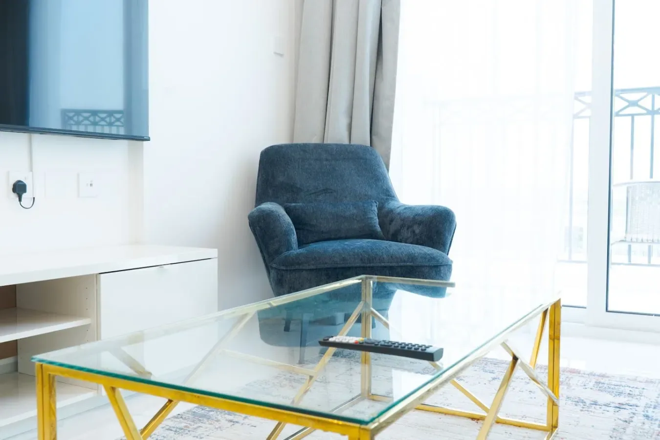 A bright living room with a blue armchair beside a glass coffee table.
