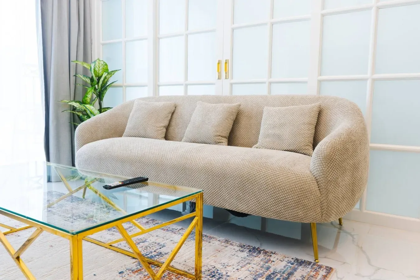 A bright living room with a beige sofa and a glass coffee table.