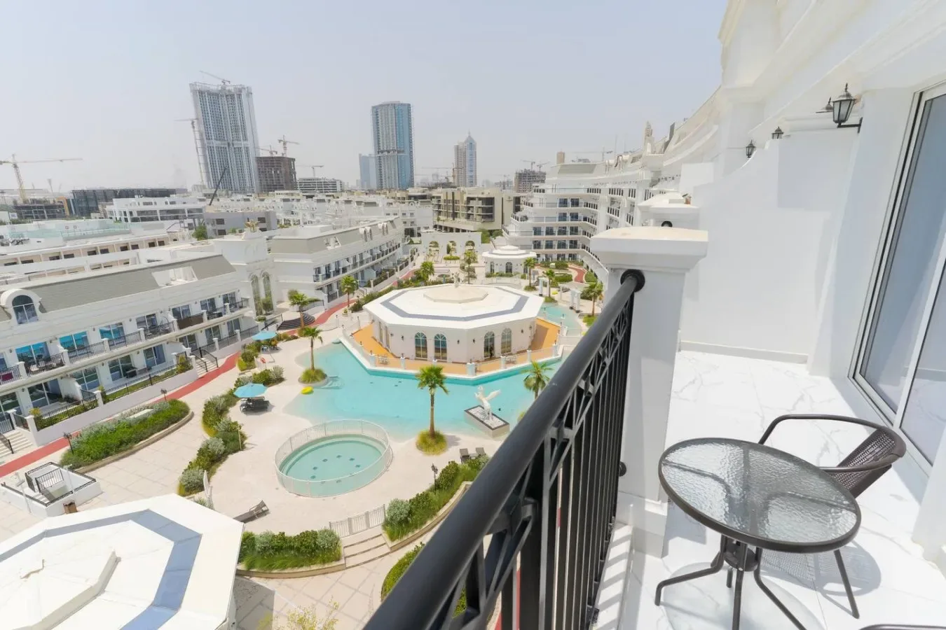 Un balcón da a un patio ajardinado con una piscina y edificios alrededor.