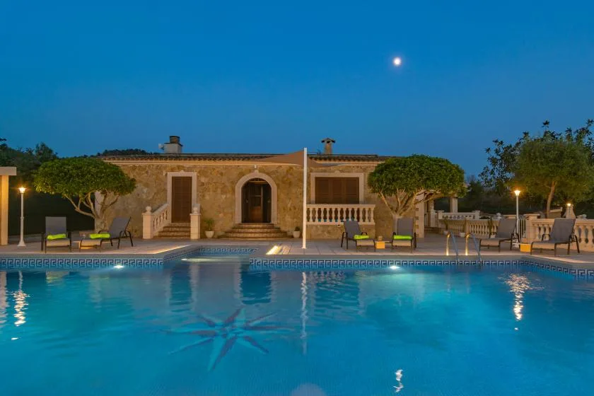 A swimming pool in front of a stone building, with outdoor seating at dusk.