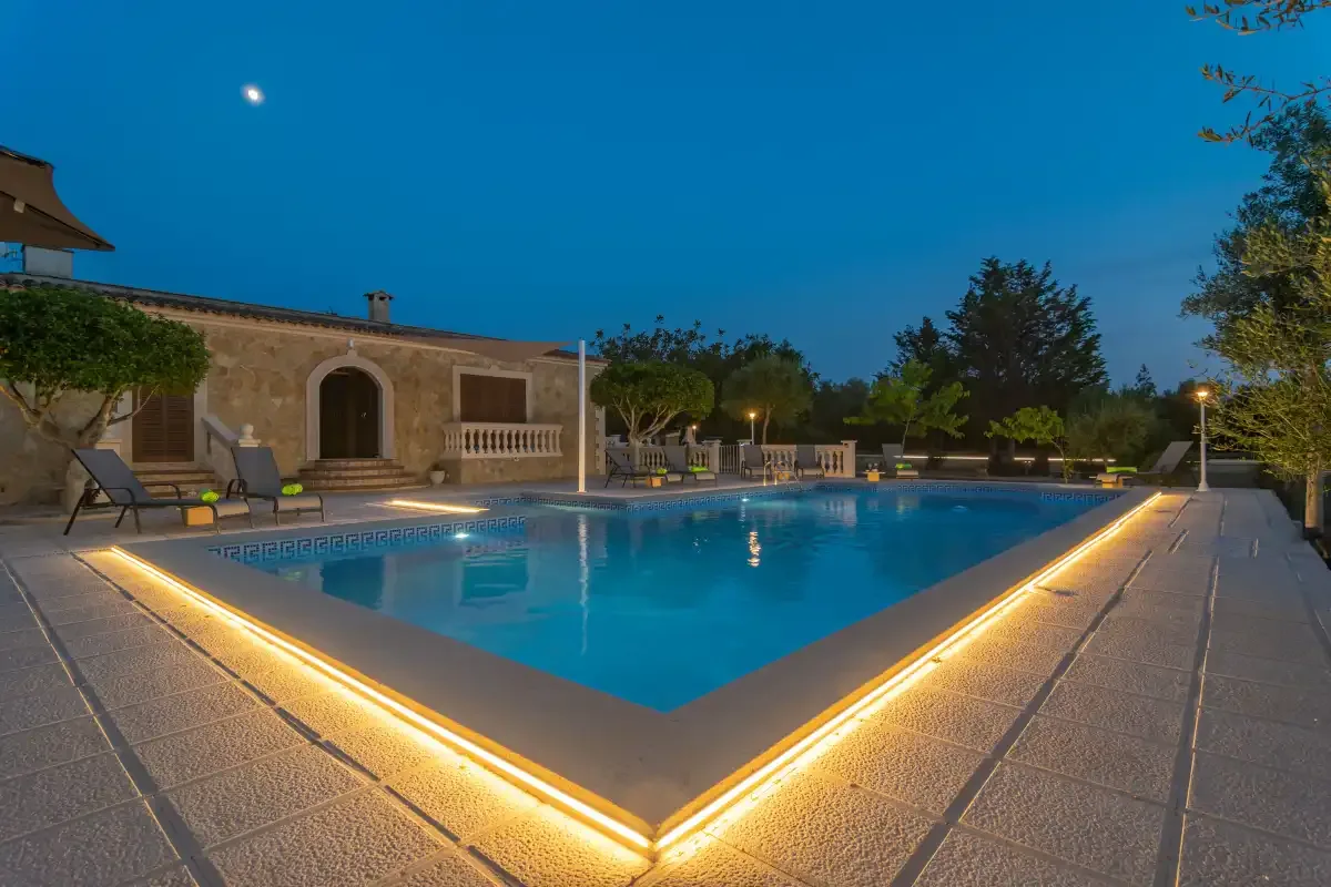 A lit outdoor swimming pool beside a stone building at dusk.