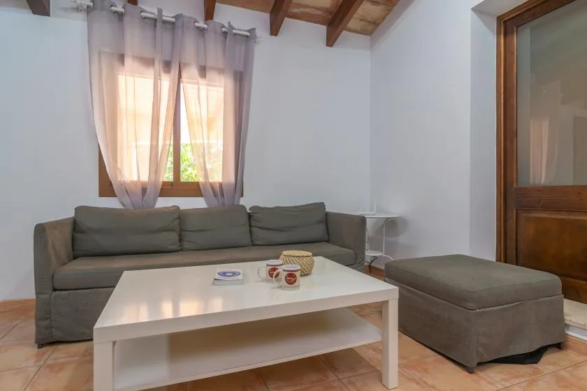A living room with seating around a white coffee table and a curtained window.