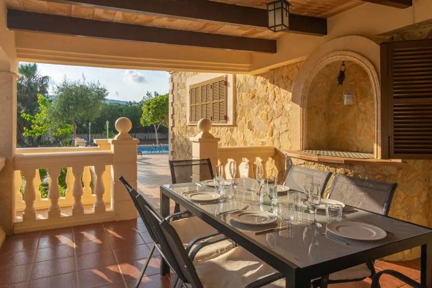 A covered outdoor dining area overlooks a pool and leafy garden.