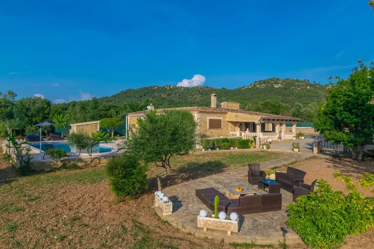 A countryside villa sits among trees, with outdoor seating and a swimming pool.