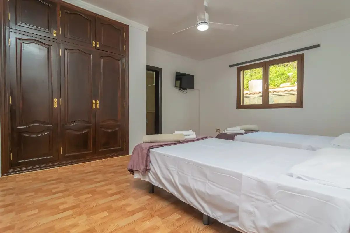 A bedroom with beds beside a large dark wooden wardrobe and a window.