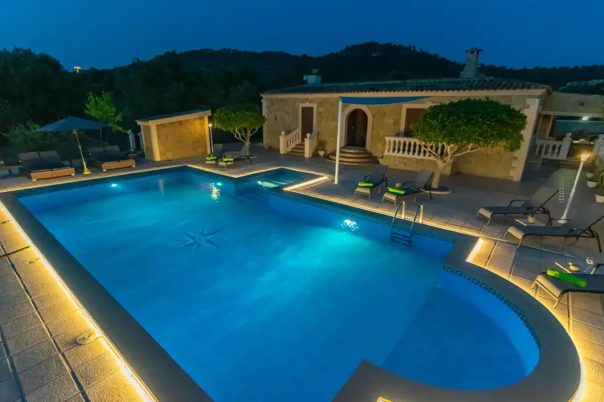 An illuminated outdoor swimming pool sits beside a low building at dusk.