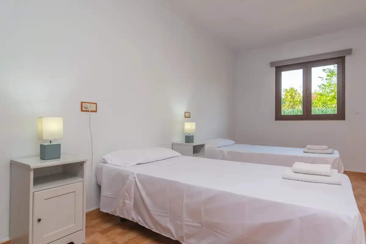 A bright bedroom with two beds and a window overlooking greenery.