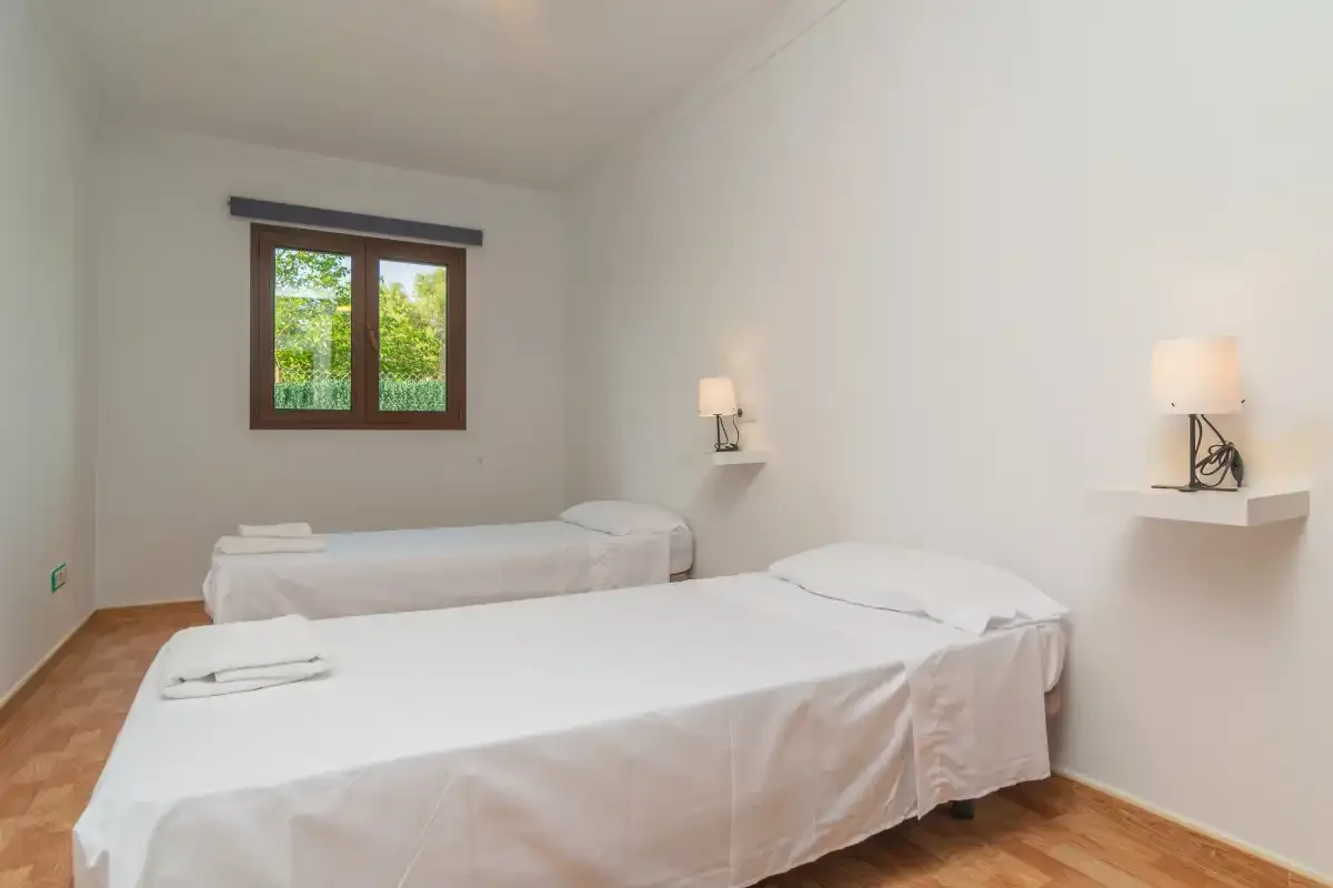 A bright bedroom with two beds and a window overlooking greenery.