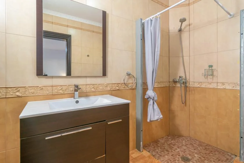 A tiled bathroom with a sink vanity, mirror, and shower.