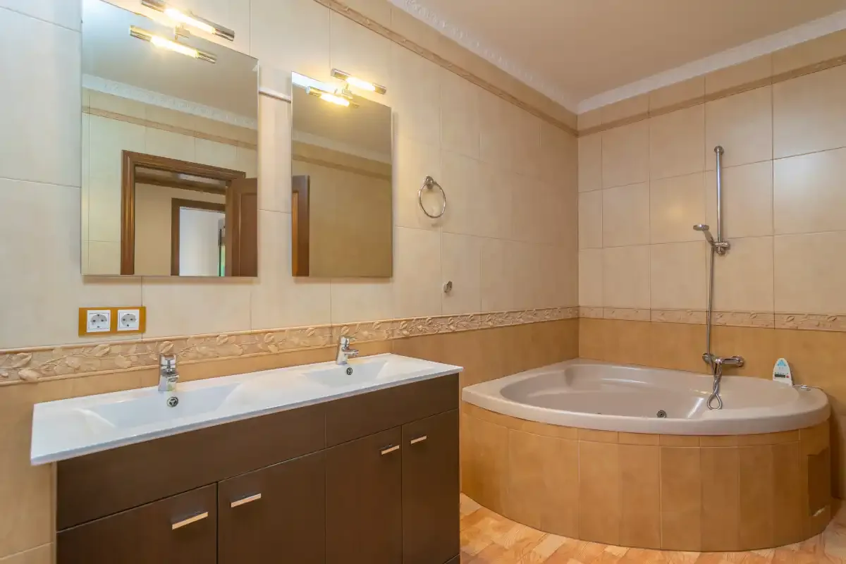 A tiled bathroom with a double sink vanity and a corner bathtub.