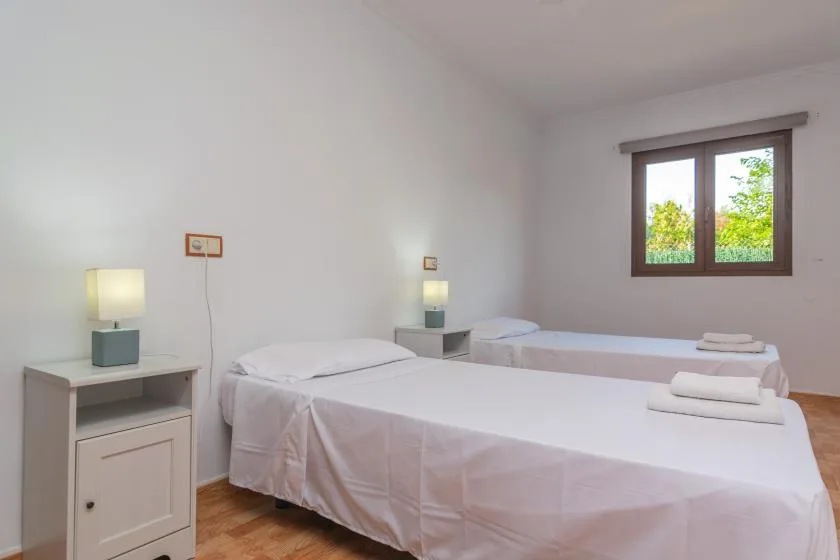 A bright bedroom with two beds and a window overlooking greenery.