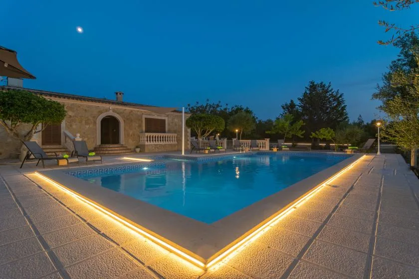 An outdoor swimming pool glows beside a stone building at dusk.
