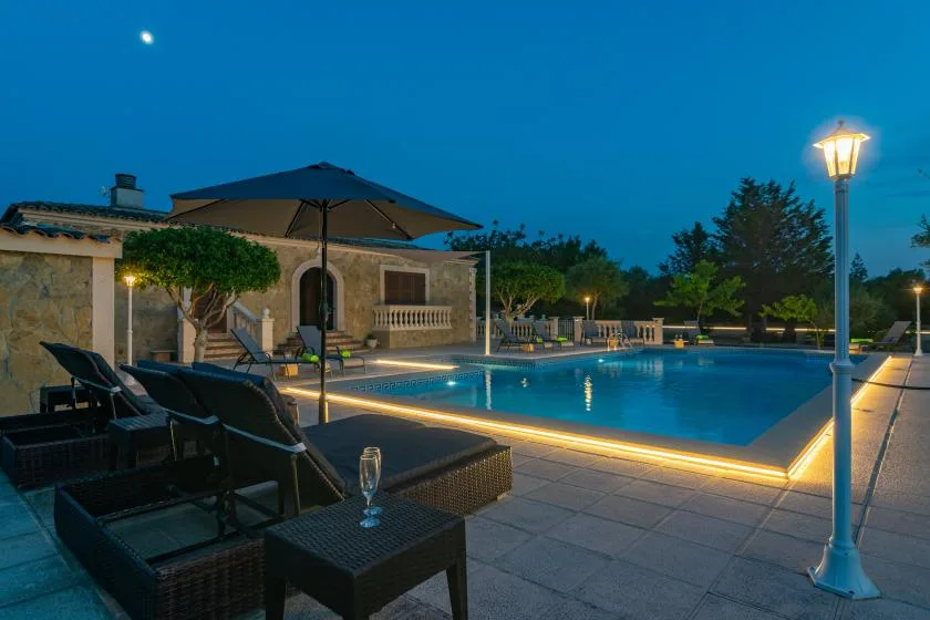 An outdoor swimming pool at dusk, with lounge seating beside the water.
