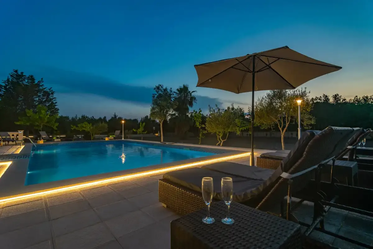 An outdoor pool and loungers sit beside a patio under the evening sky.