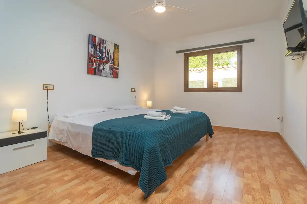A bedroom with a bed covered by a teal blanket and a window.