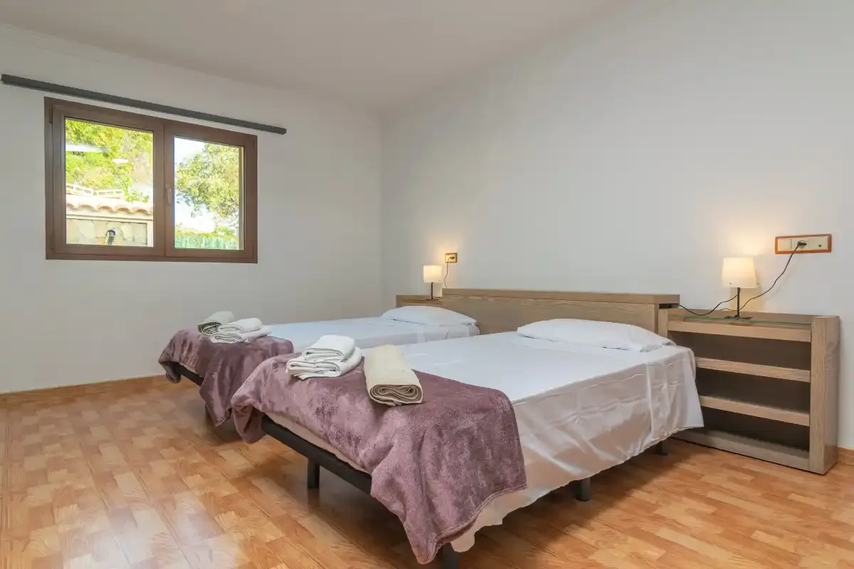 A bedroom with two beds, folded towels, and a window overlooking greenery.