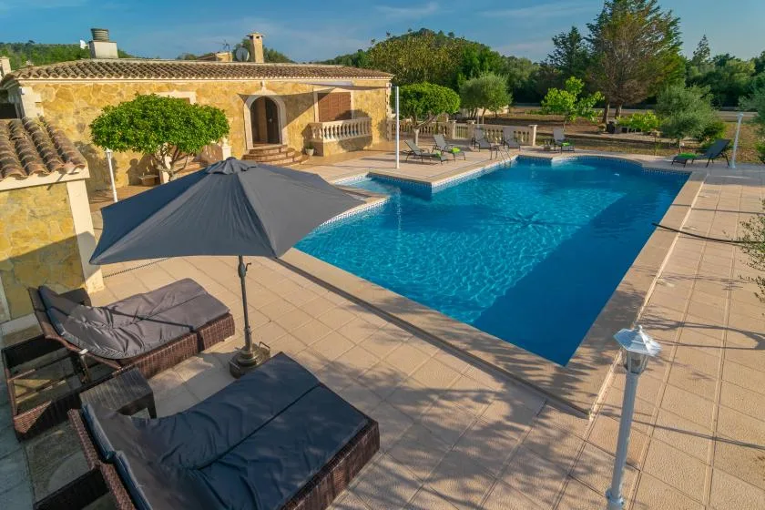 A swimming pool beside a stone building, with shaded seating on the surrounding patio.