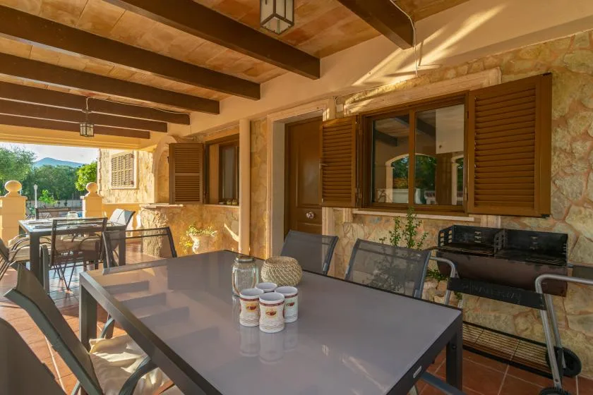 A covered outdoor dining area with a table and windows with wooden shutters.