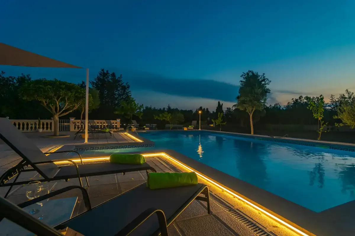 A swimming pool glows beside lounge seating at dusk.