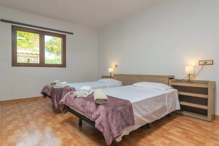 A bedroom with two beds, folded towels, and a window.
