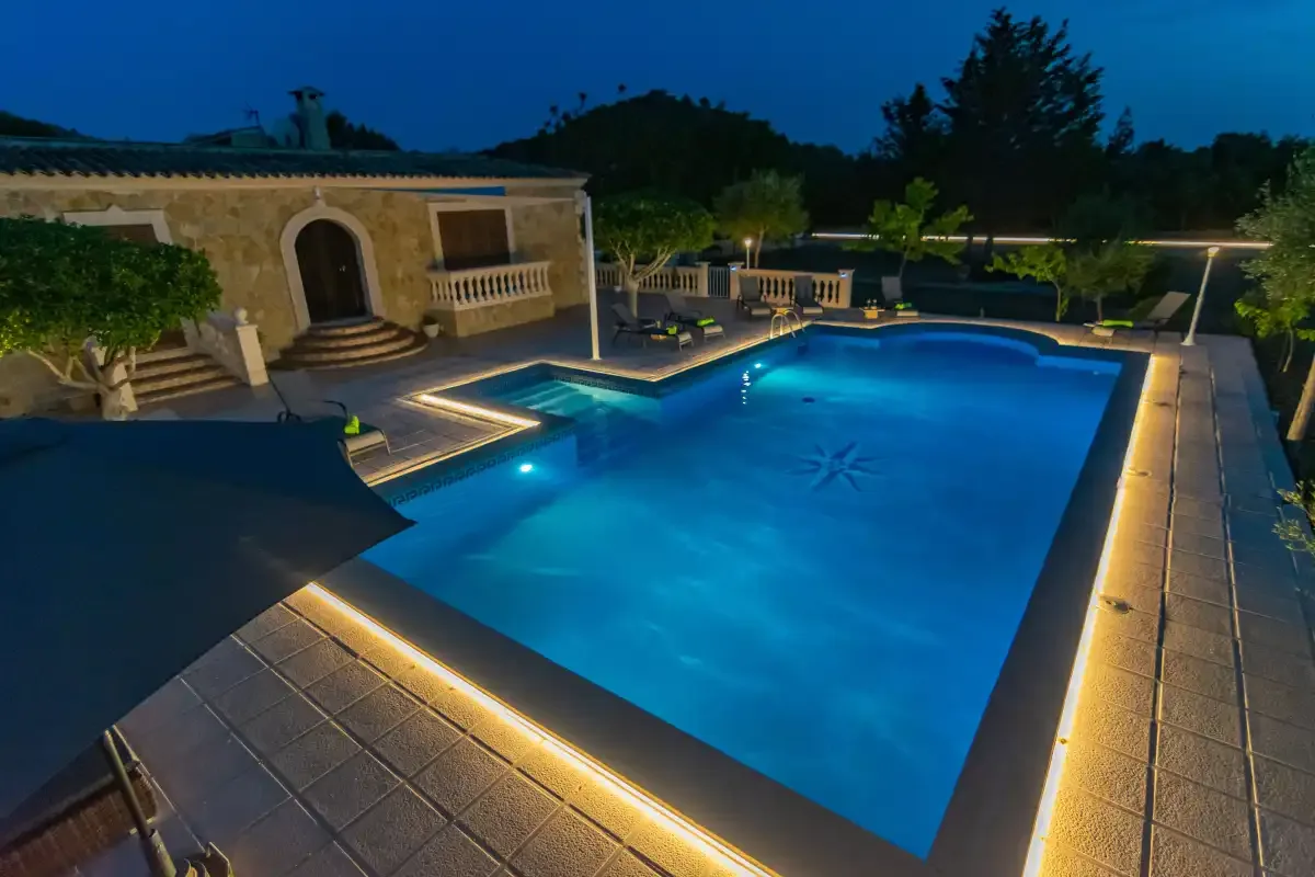 An illuminated outdoor swimming pool beside a stone building at dusk.