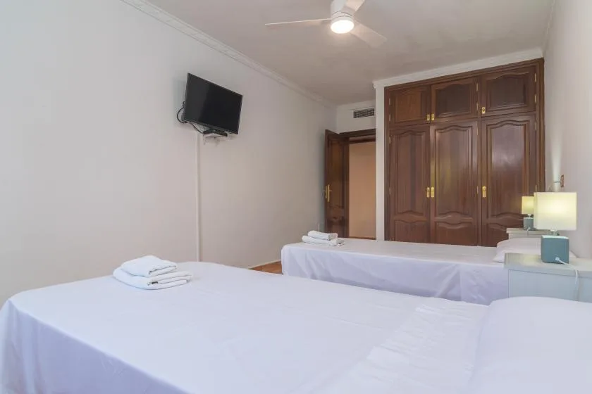 A bedroom with white-covered beds, a wall-mounted television, and a wooden wardrobe.