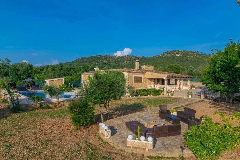 A countryside property with a swimming pool and outdoor seating beneath green hills.