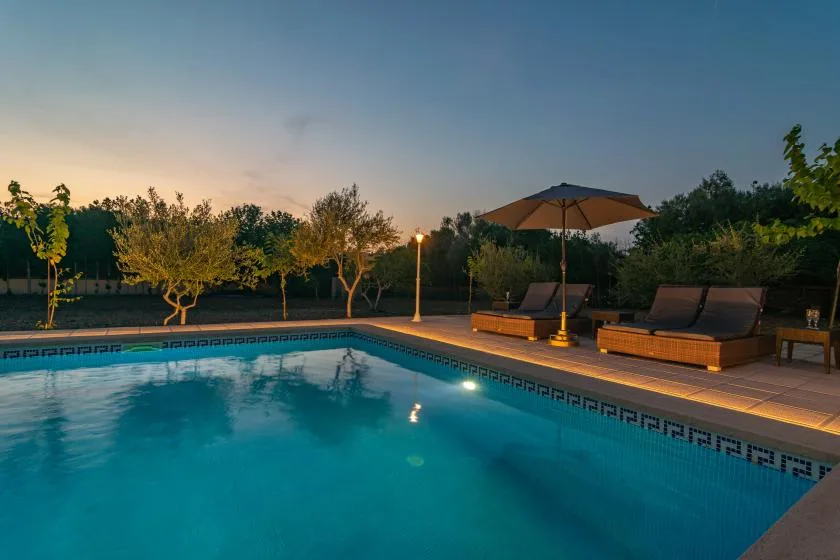 An outdoor swimming pool beside a tiled deck with lounge seating and an umbrella.