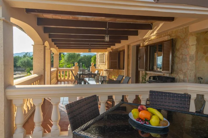 A covered terrace with outdoor seating and a bowl of fruit on the table.