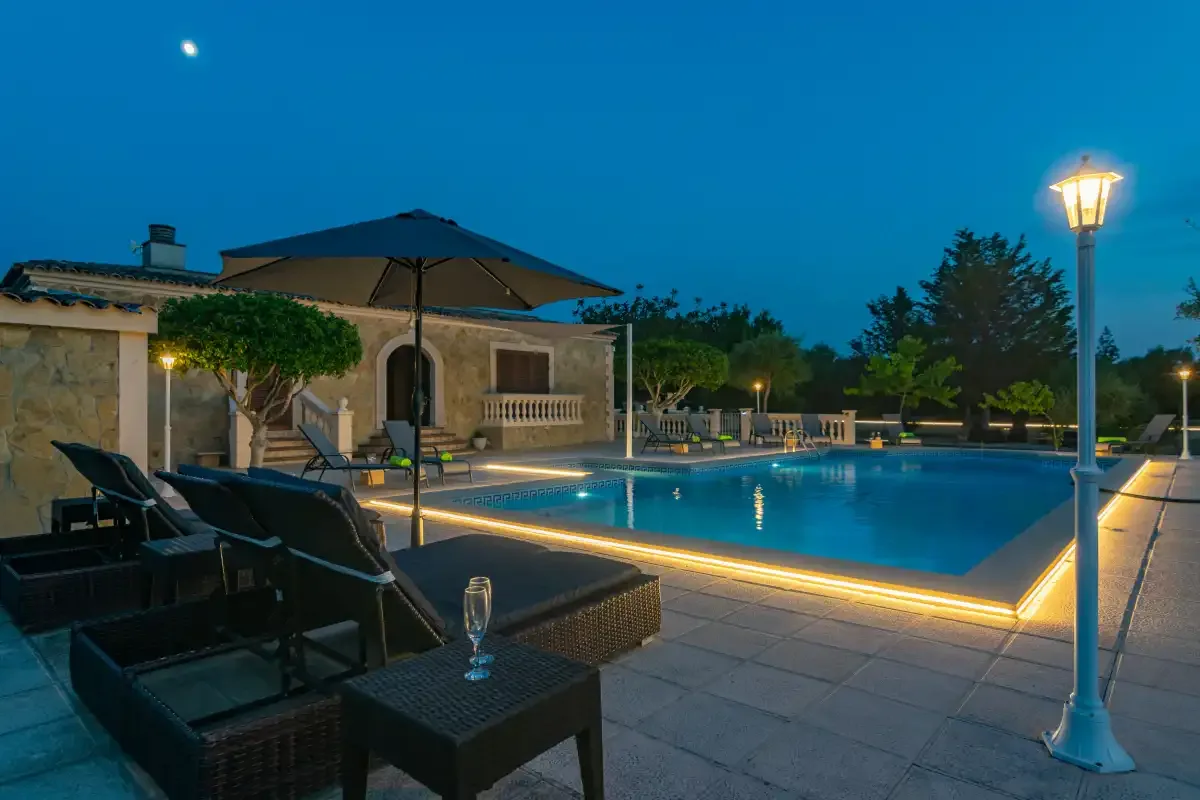 An outdoor swimming pool glows beside patio seating at dusk.