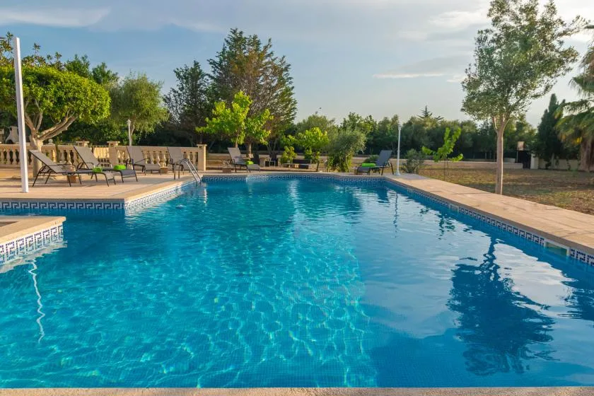 An outdoor swimming pool is surrounded by lounge seating and greenery.