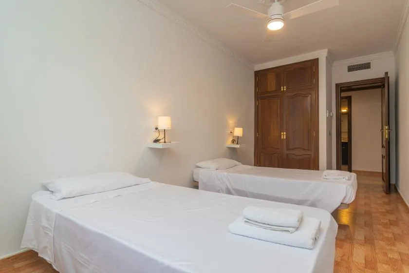 A bedroom with two beds, wall lights, and a wooden door.