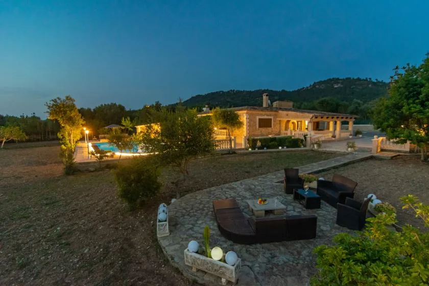 An outdoor patio with seating overlooks a lit pool and a low building at dusk.