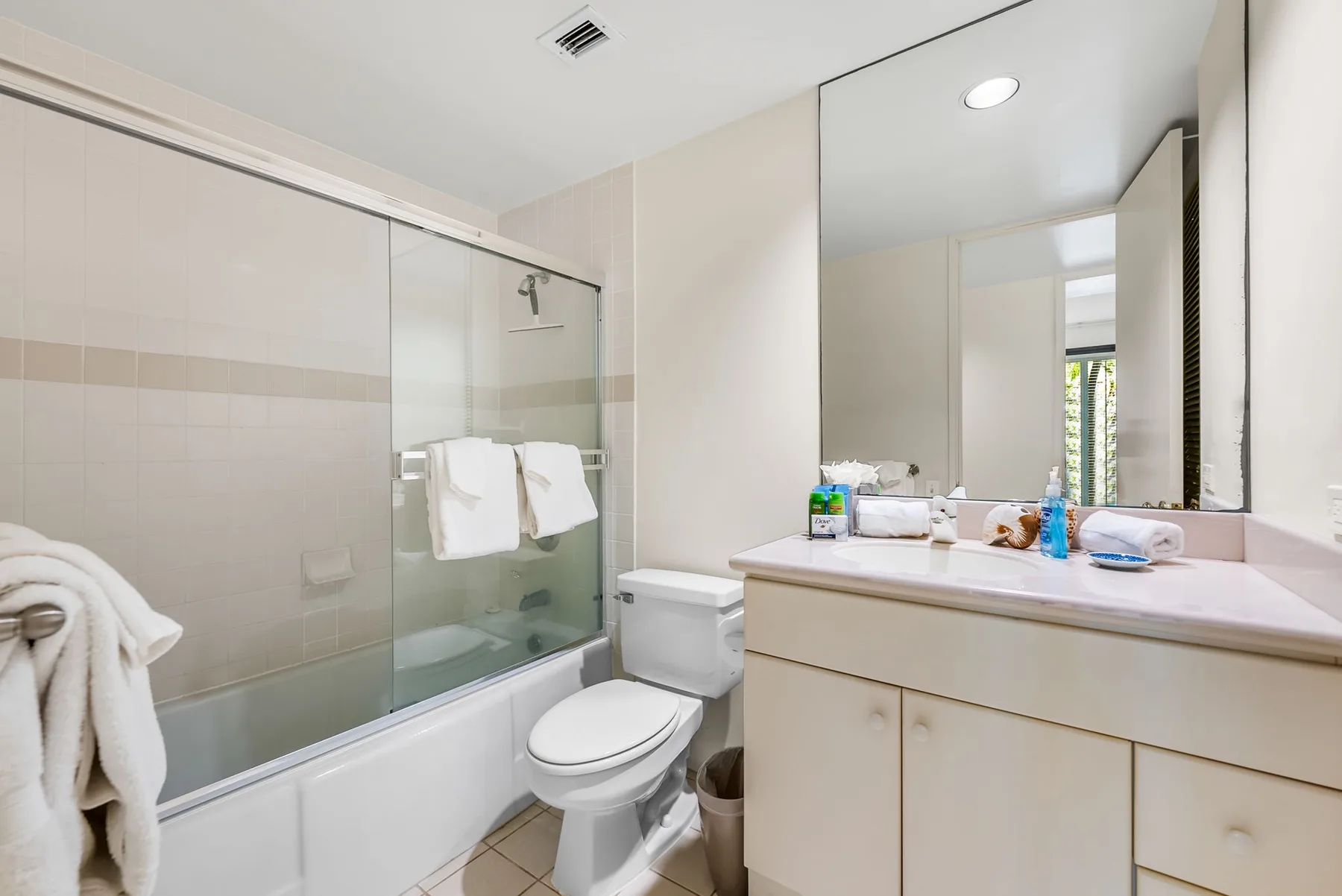 A bright bathroom with a glass shower, toilet, and sink vanity.