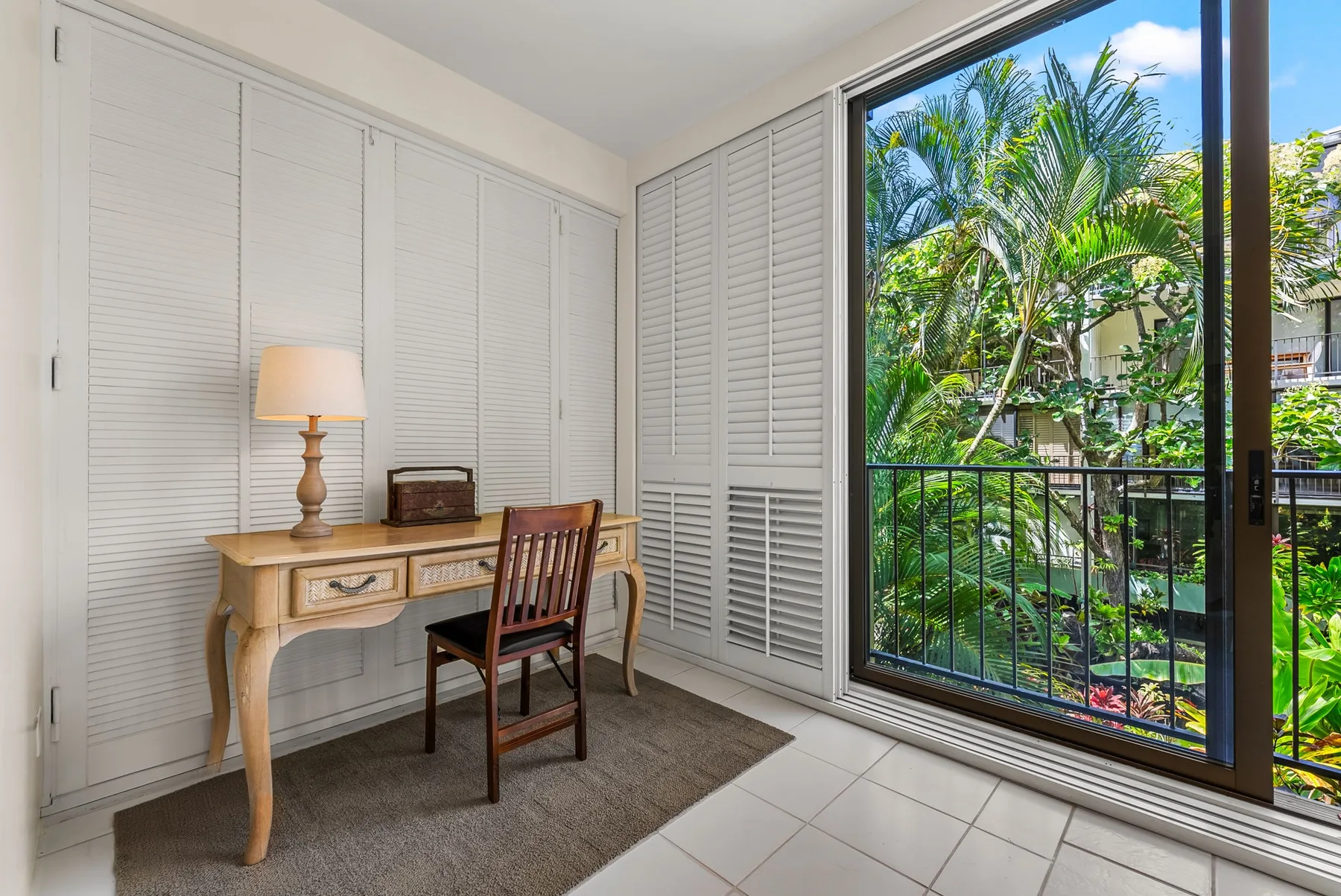 A desk and chair sit beside a large window overlooking leafy greenery.