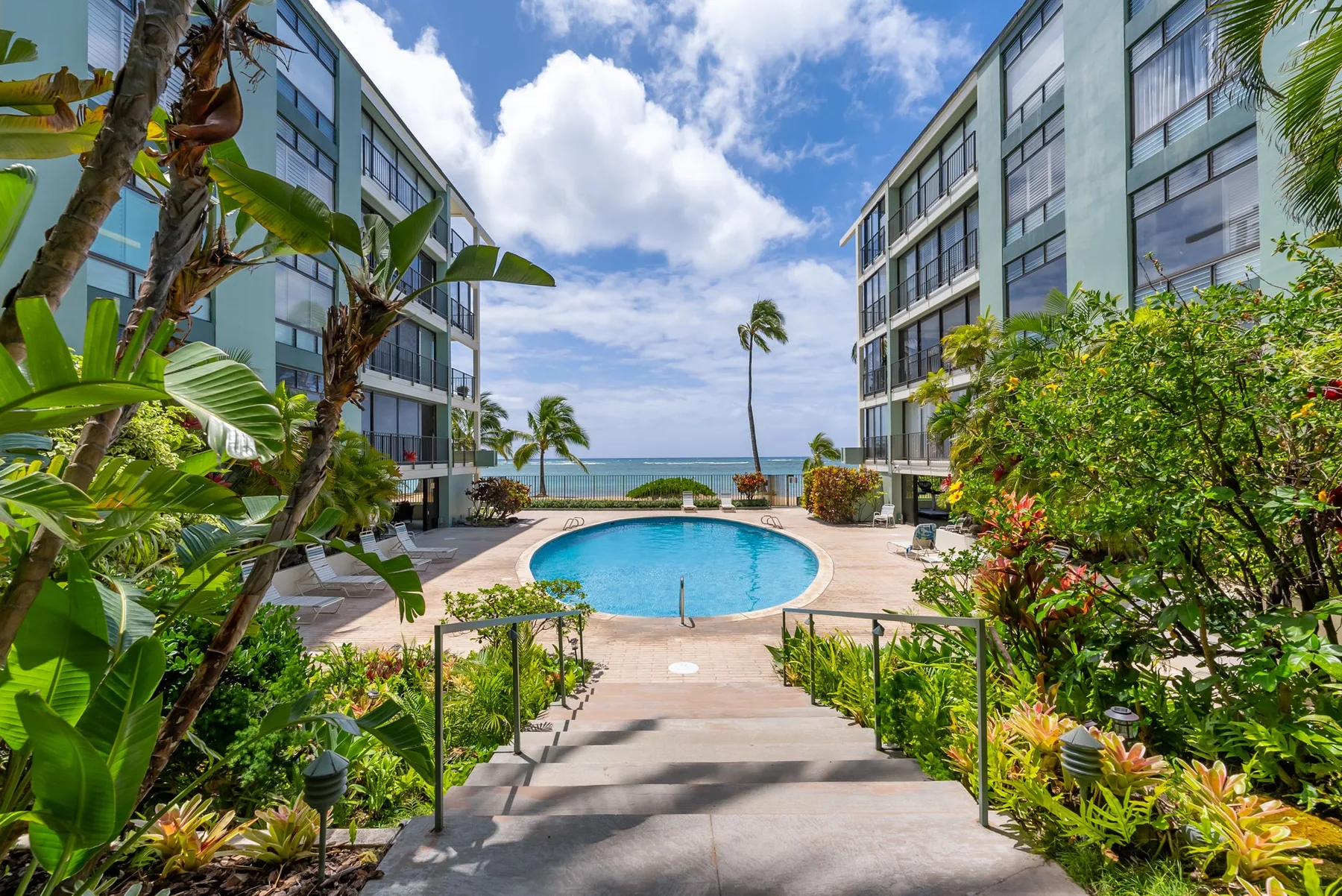A courtyard pool sits between two buildings, with the ocean visible beyond.