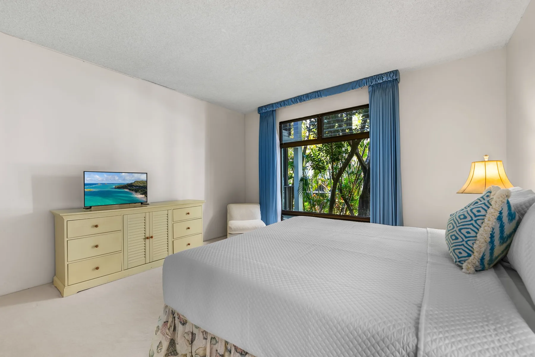A bedroom with a neatly made bed beside a window framed by blue curtains.