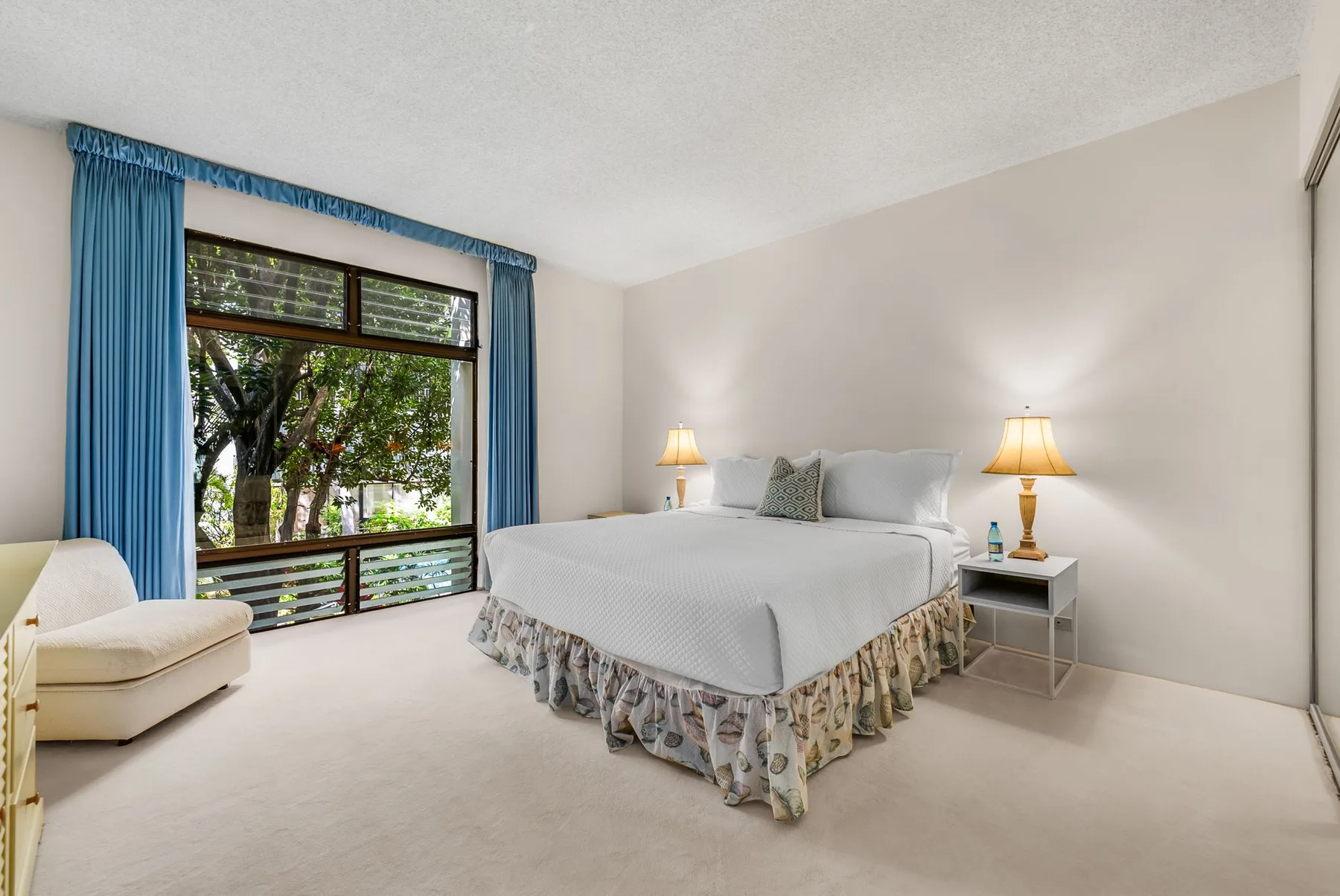 A bedroom with a large bed, bedside lamps, and a window framed by blue curtains.