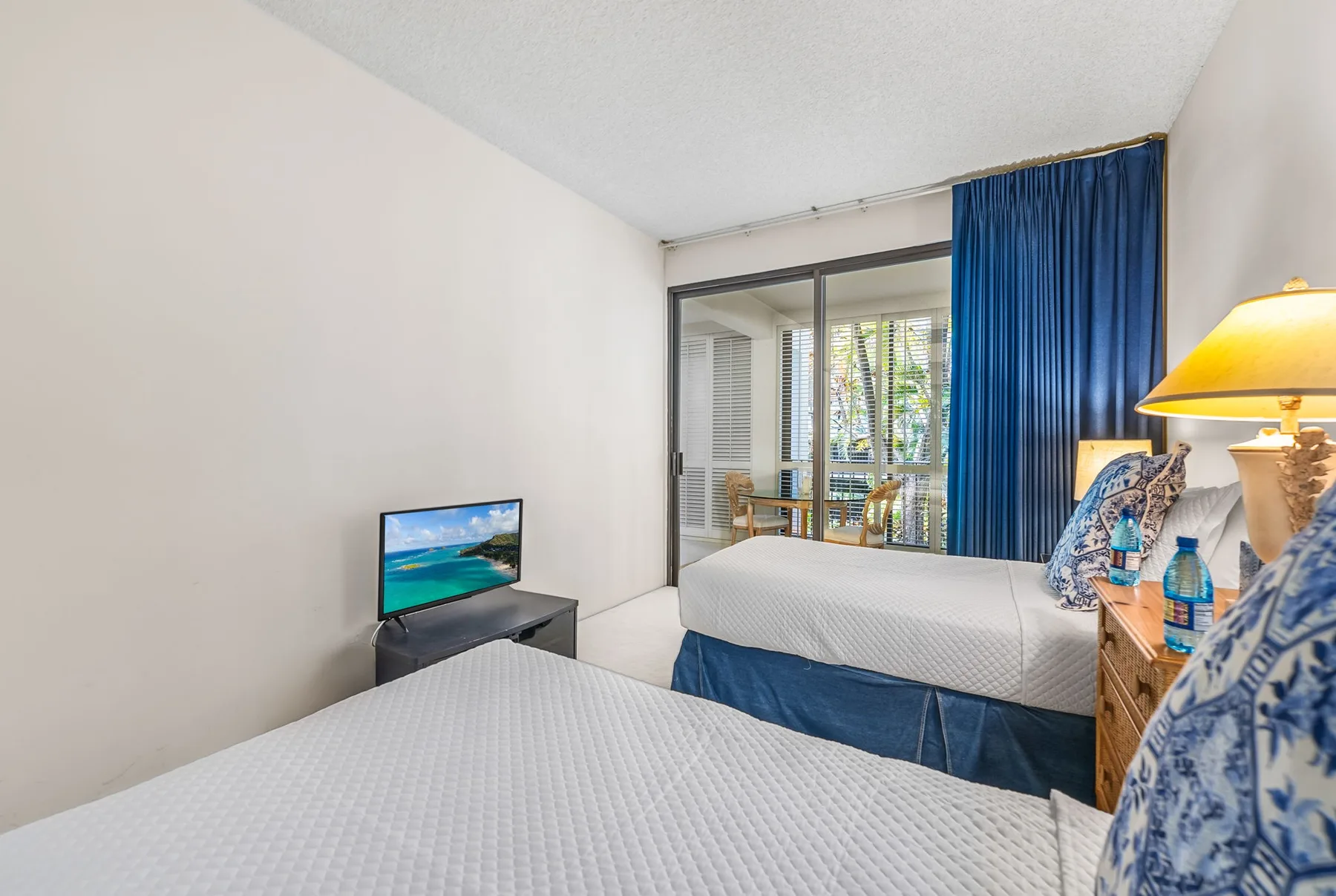 A bedroom with two beds, a television, and sliding glass doors.