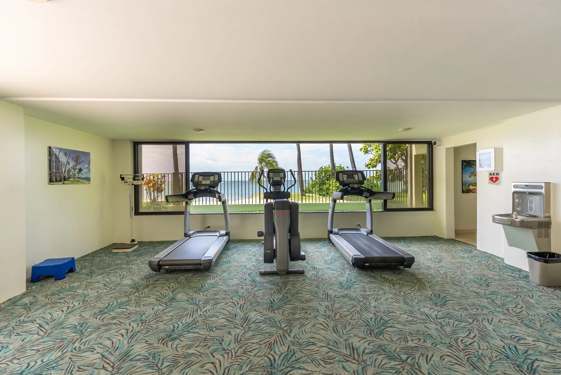 A fitness room with exercise machines facing large windows overlooking the water.