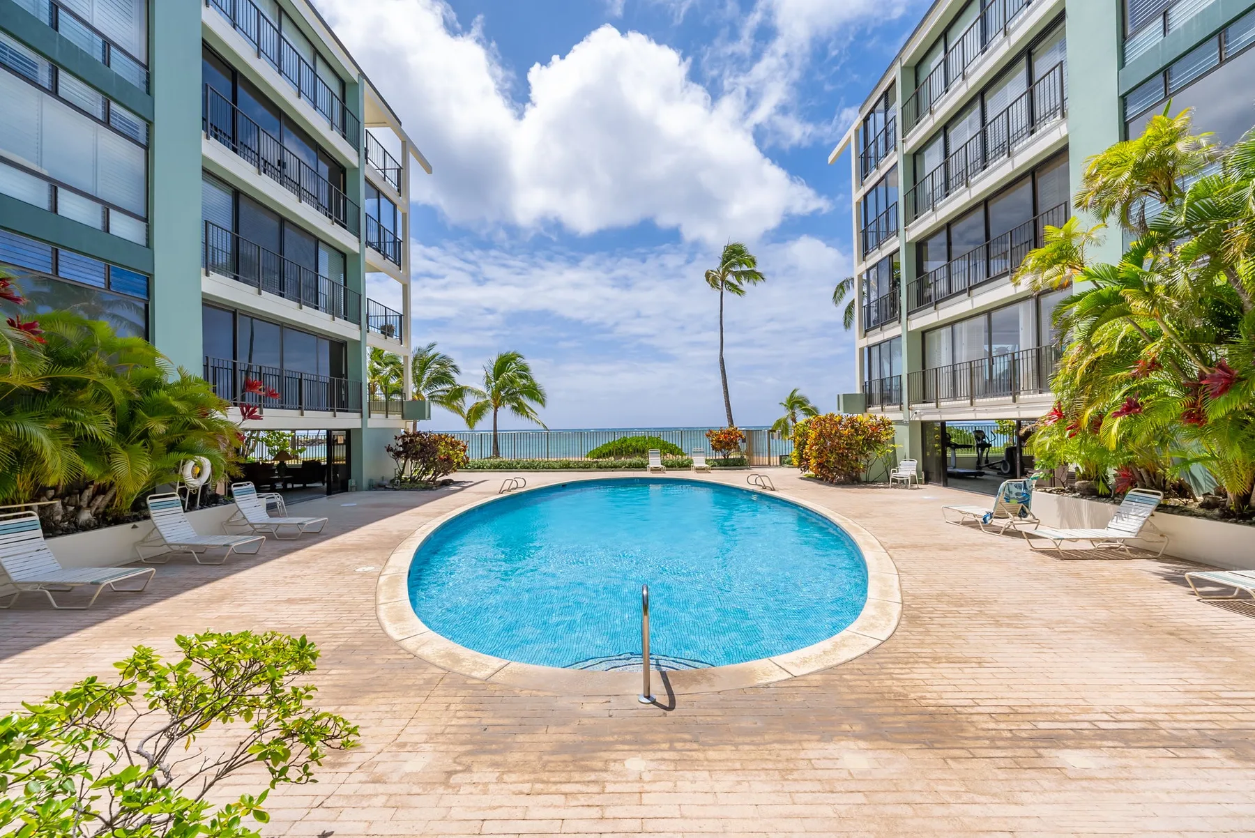 An outdoor swimming pool sits between two buildings, with lounge seating nearby.