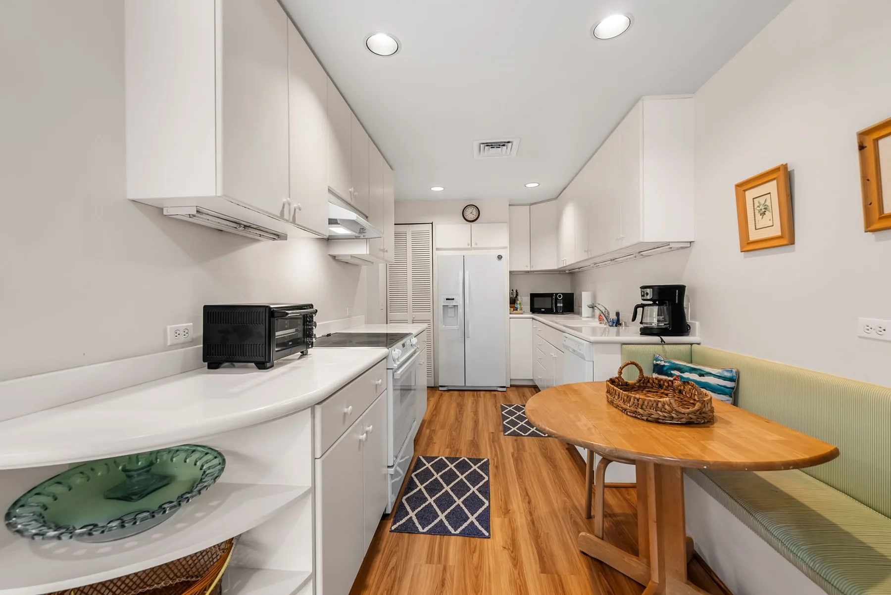 A bright kitchen with white cabinets, wood flooring, and a round dining table.