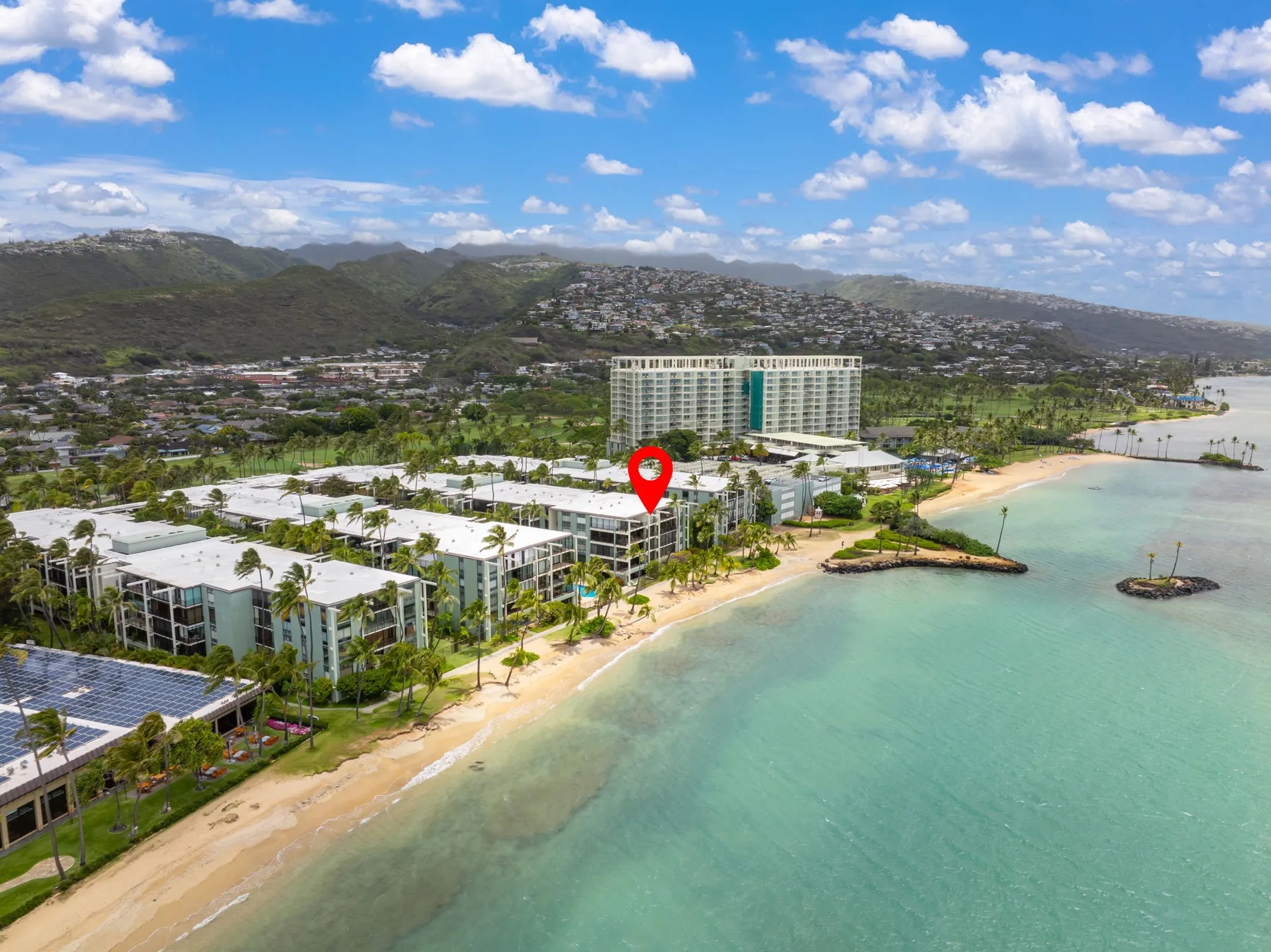 Aerial view of a beachfront resort beside turquoise water and green hills.