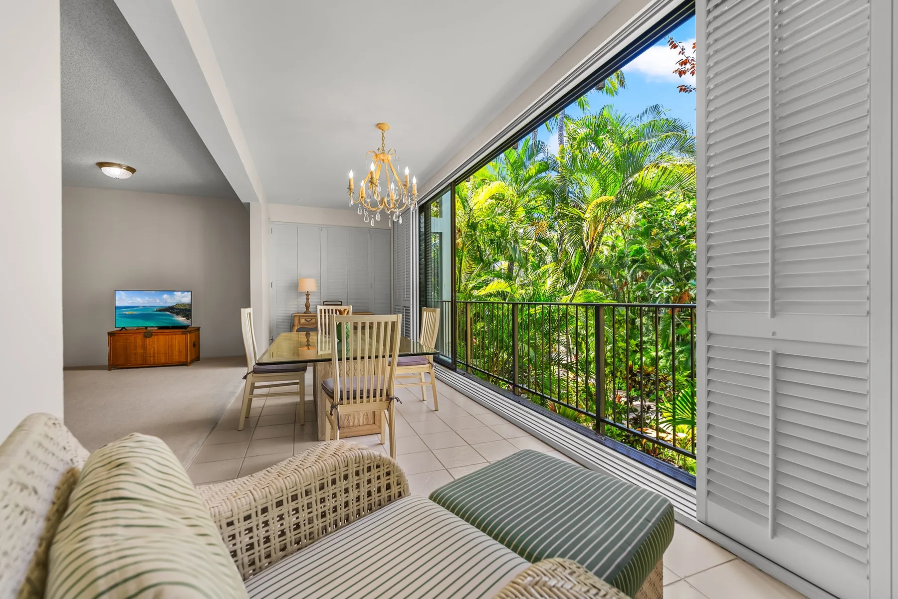 A bright sitting and dining area opens onto a balcony overlooking lush greenery.