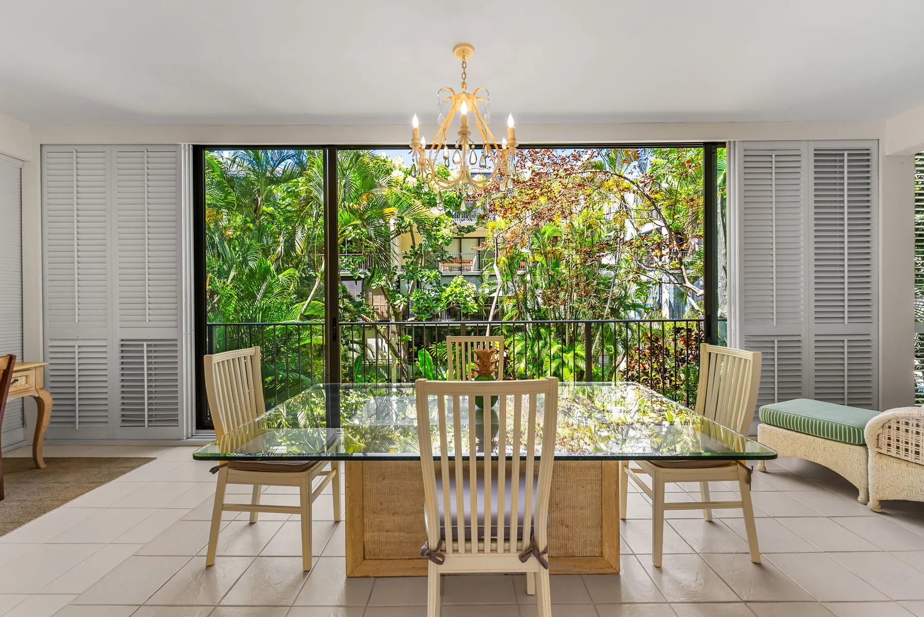 A dining area with a glass table and leafy greenery visible through the windows.